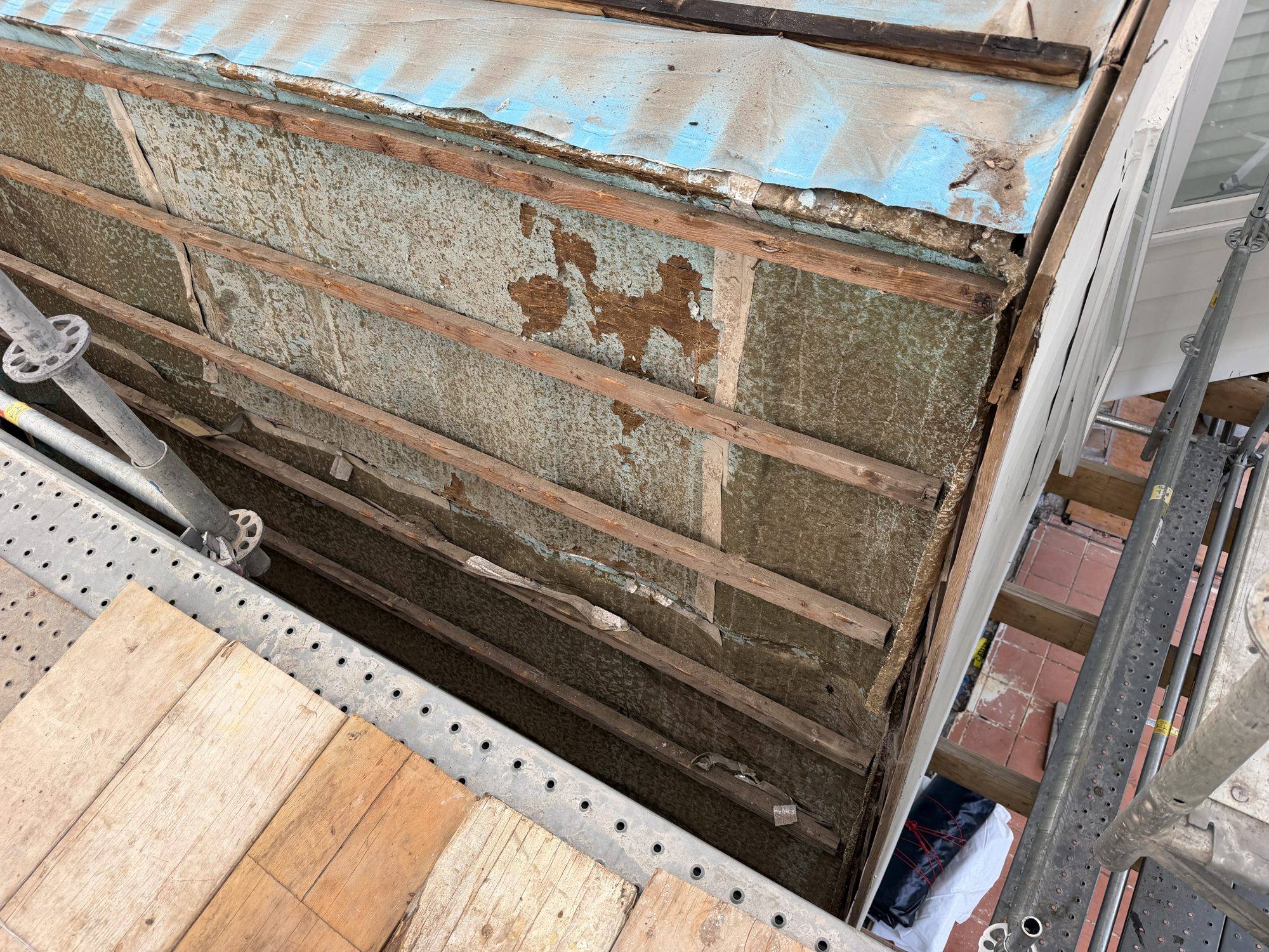 Original fibro wall cladding exposed mid-removal behind scaffold
