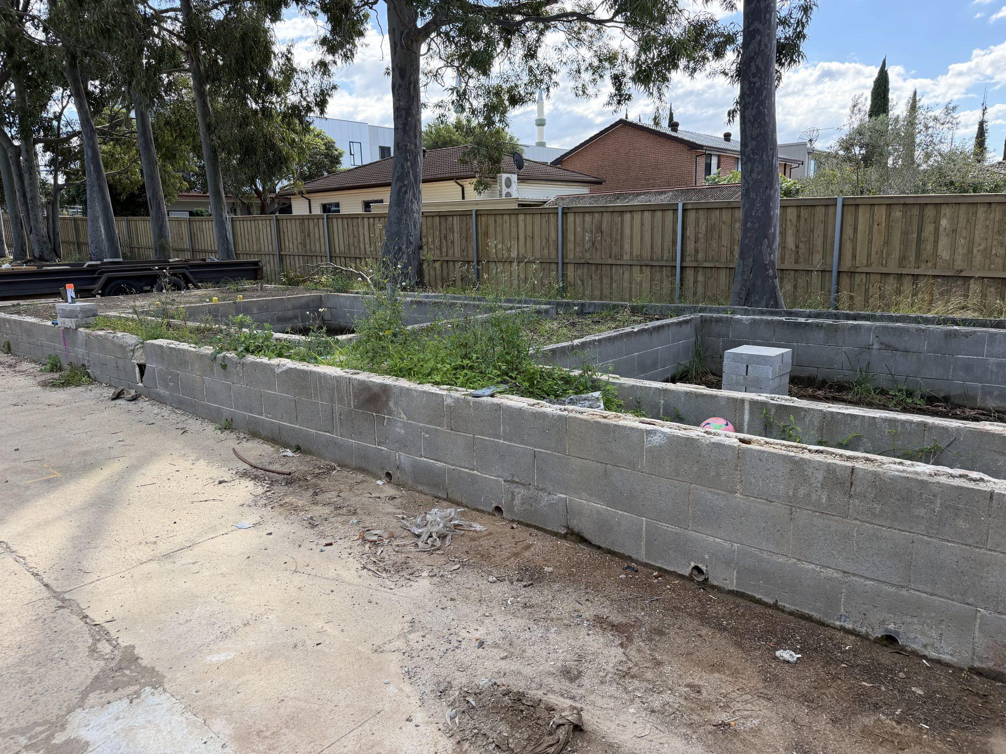 The full run of concrete block planter beds along the fence line before demolition